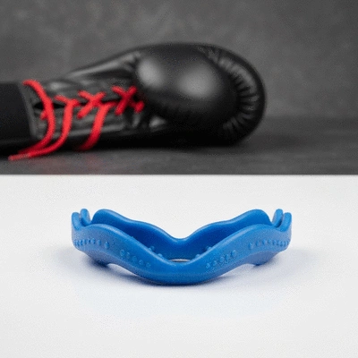 Close-up of a mouthguard lying on a clean surface with boxing gloves in the background, clean product shot